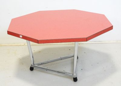 une petite table au plateau rouge posée sur un sol blanc