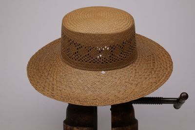 un chapeau de paille posé sur un support en bois, surmonté d'un autre chapeau
