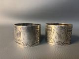 two silver napkin rings with initials on them sitting next to each other