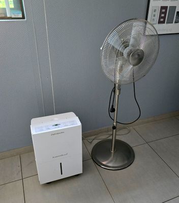 un ventilateur posé à côté d'une boîte blanche sur un sol carrelé
