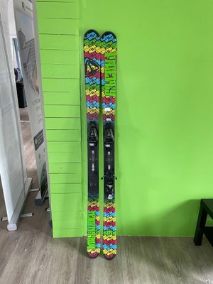 des skis et des bâtons de ski appuyés contre un mur vert, devant un mur vert