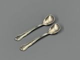 two silver spoons sitting on top of a table next to each other
