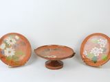 three small plates with flowers painted on them sit on a stand