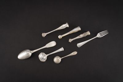 six cuillères en argent et une fourchette posées sur un fond noir