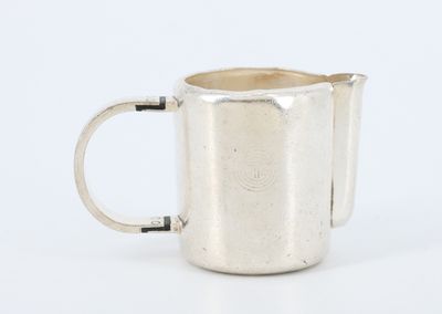 une vieille coupe en argent munie d'une anse, posée sur une surface blanche