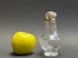 an apple next to a glass salt and pepper shaker