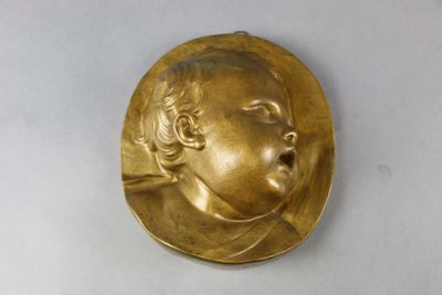 plaque en laiton représentant le visage d'un bébé sur fond blanc