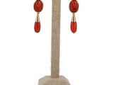 une paire de boucles d'oreilles rouges et dorées posées sur un présentoir