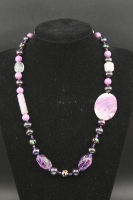 un collier composé de perles violettes et d'un disque blanc, présenté sur un mannequin noir