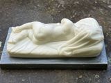 une statue représentant une femme allongée sur un drap posé à même le sol