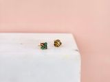 un gros plan sur une paire de boucles d'oreilles dorées et vertes posées sur un bloc de marbre