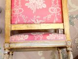 a small wooden chair with a pink seat on a bed