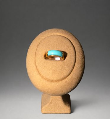 une image représentant une bague posée sur un présentoir, avec une pierre turquoise au centre