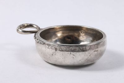 une vieille coupe en argent munie d'une anse, posée sur une surface blanche