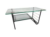 La table en verre est dotée d'un piètement en métal et d'un plateau en verre.