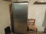 a silver refrigerator and a chair in a dirty room