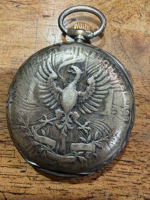 an old pocket watch with a bird on it sitting on a wooden table