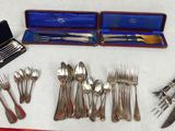 a lot of silverware on a table with a red cloth