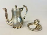 une théière en argent et une bague en argent posées sur une table