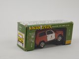 un petit camion-jouet dans une boîte, posé sur une surface blanche, avec un fond blanc