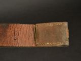 an old brown leather belt with a metal buckle on a black background