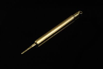 une image représentant un stylo en métal de couleur dorée sur fond noir