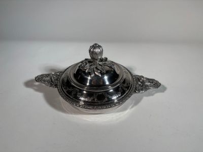 un plat ancien en argent avec un couvercle, posé sur une surface blanche