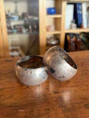two silver bowls sitting on a table with a bookcase in the background