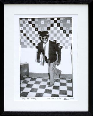 black and white photograph of a man in a suit and tie standing in front of a checkered wall