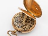 a gold pocket watch that is open on a white surface