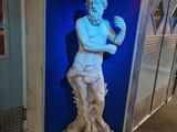 une statue représentant un homme debout devant un mur bleu