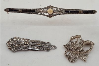 trois bijoux argentés et noirs posés sur une surface blanche