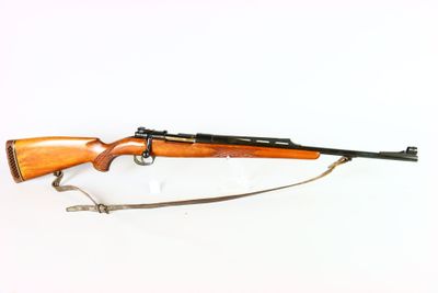 un vieux fusil au canon en bois, muni d'une bretelle, posé sur une surface blanche