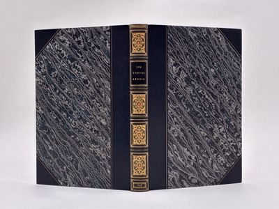 un vieux livre à la couverture noire et aux bordures dorées posé sur une surface blanche