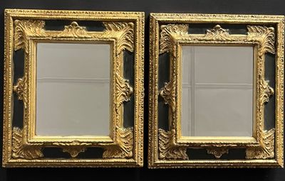 two gold framed mirrors on a black wall in a room