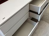 un bureau blanc à deux tiroirs, avec une chaise rouge en arrière-plan
