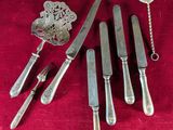 five knives, a spoon, and a spoon rest on a red cloth