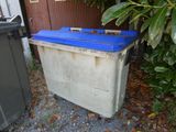 une poubelle posée à côté d'une autre poubelle devant un immeuble