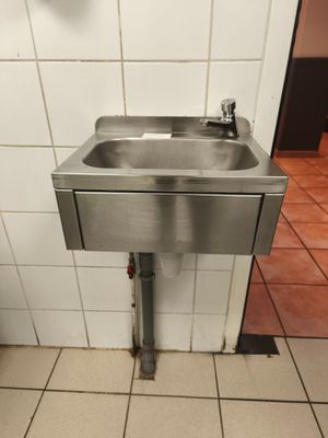 un lavabo en acier inoxydable dans des toilettes publiques aux murs carrelés