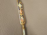 a gold and blue knife sitting on top of a leather surface