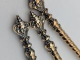 two antique silver spoons with ornate designs on them on a white surface