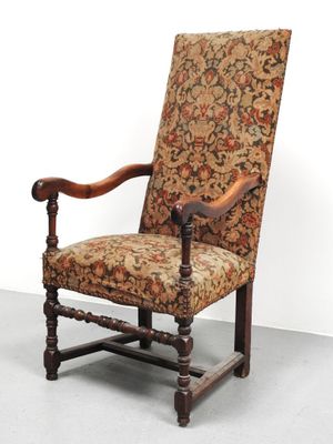 une vieille chaise avec un dossier et des accoudoirs tapissés de fleurs