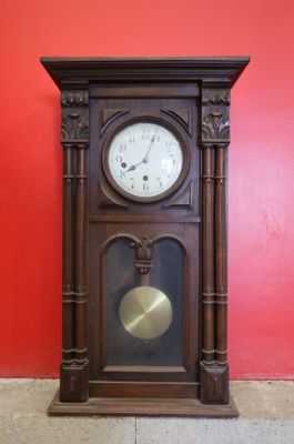 une horloge posée par terre devant un mur rouge