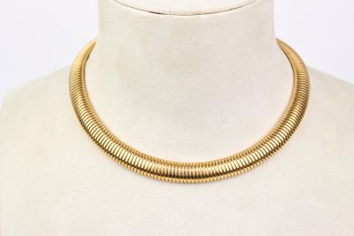 Le collier est en métal doré et présente un motif imitant la peau de serpent.