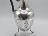 an antique silver plated pitcher on stand with a black handle