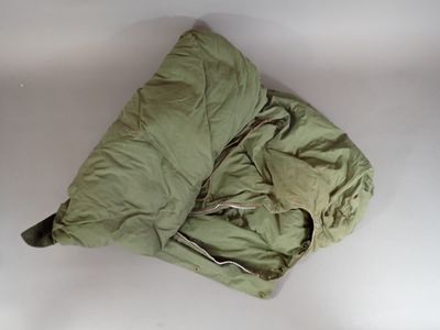 a green sleeping bag on a white surface next to a pillow