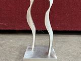 silver sculpture of two wavy shapes on a marble base on a red background