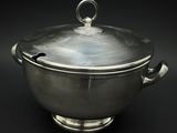 casserole plaquée argent avec couvercle, posée sur un support, sur fond noir