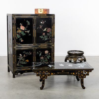 une armoire noire décorée de fleurs et une petite table sur laquelle se trouve un bol