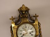 a gold clock on a white wall with roman numerals on it